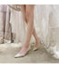 Silver high-heeled shoes worn with a white dress against a neutral background