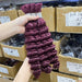 Burgundy hair extensions held by a hand with boxes of hair extensions in the background