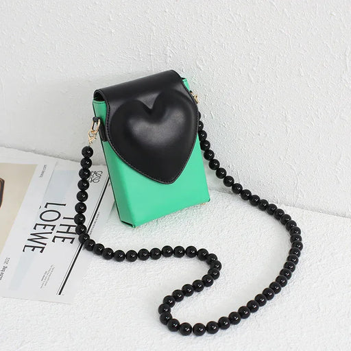 Green handbag with black heart-shaped pouch and beaded strap on a white surface.