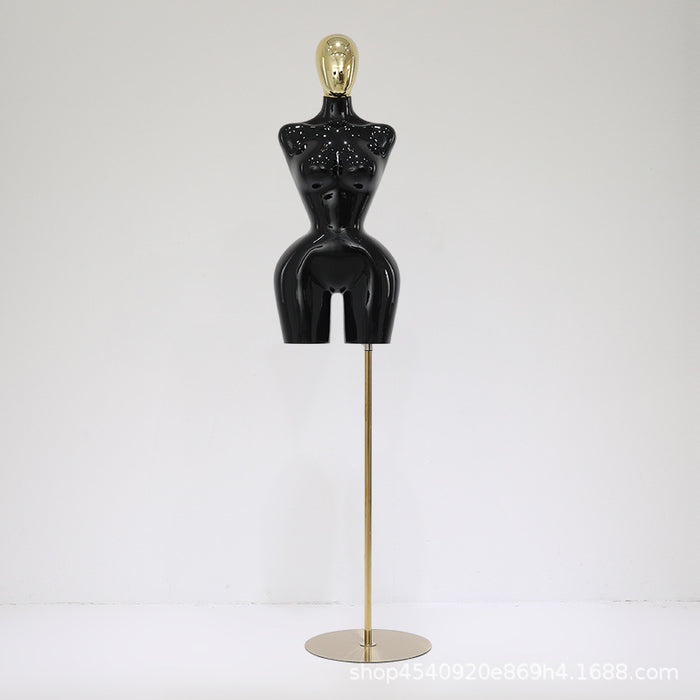 Black mannequin torso on a gold stand against a white background