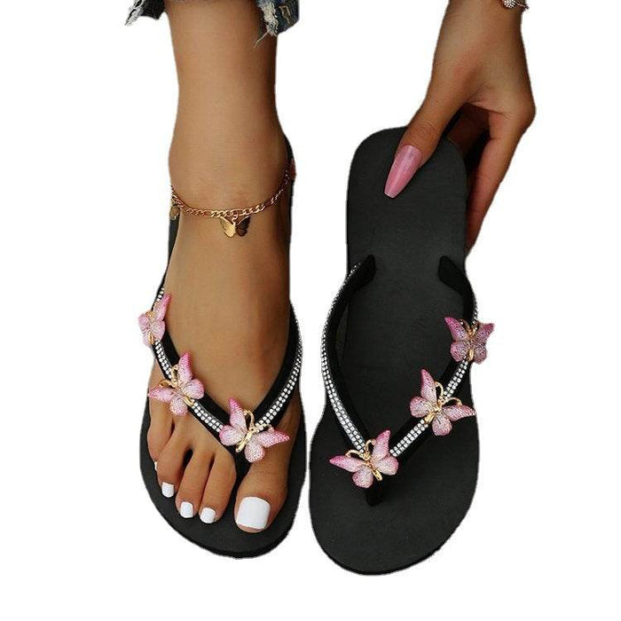 Black flip-flops with pink butterfly decorations on a white background