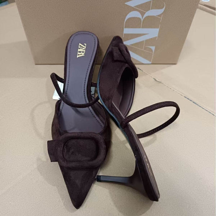 Pair of brown high-heeled shoes with a bow detail on a beige surface, with a Zara box in the background.