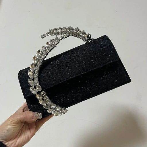 Black glittery handbag with decorative handle held by a hand against a light background