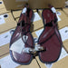 Pair of maroon sandals with gold accents on a cardboard box background