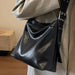 Black leather handbag held by a person wearing a beige coat indoors.