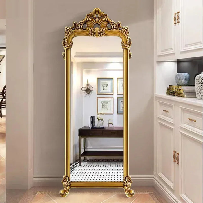 Gold ornate full-length mirror in a room with white cabinets and decor.