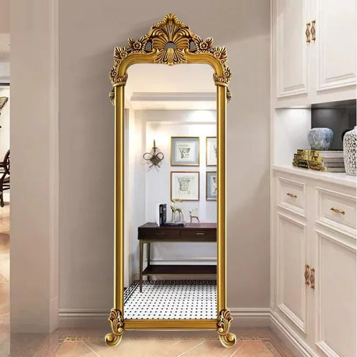 Gold ornate full-length mirror in a room with white cabinets and decor.