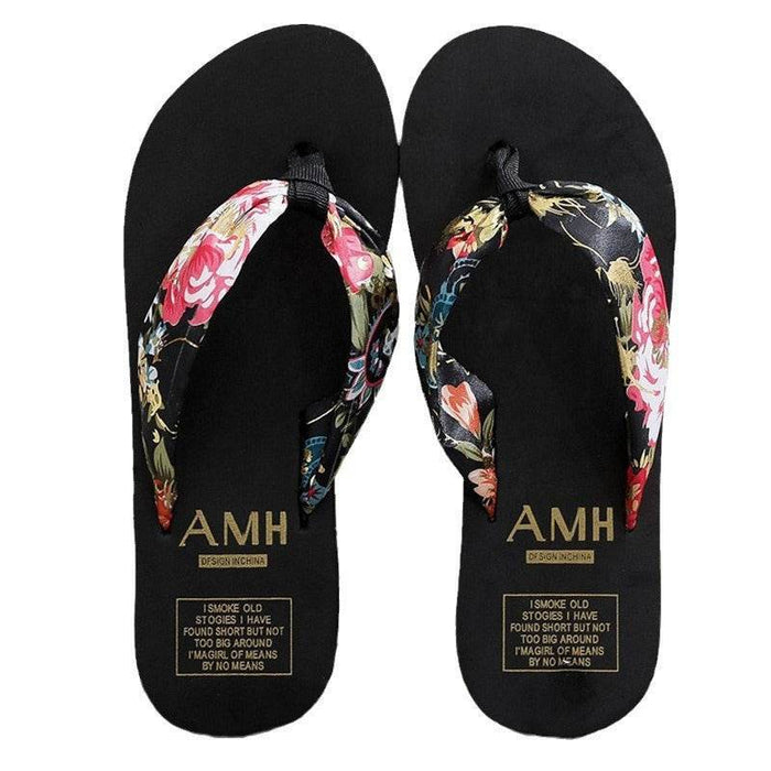 Black flip-flops with floral straps and 'AMH' branding on a white background