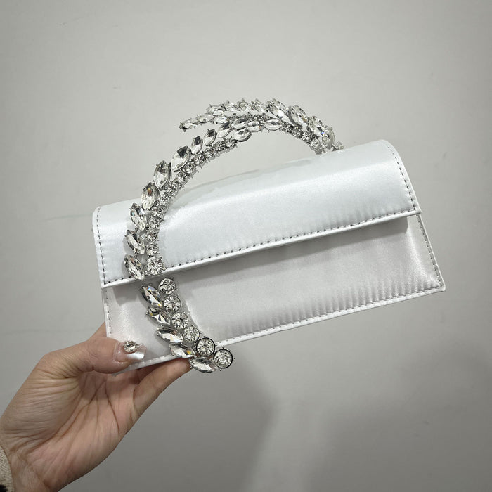 White handbag with decorative silver chain held by a hand against a gray background