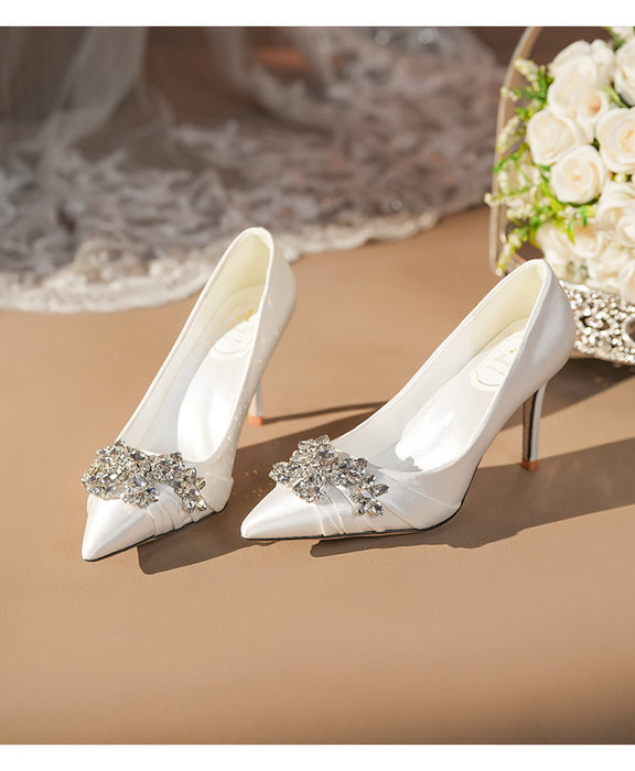 White high-heeled shoes with decorative elements on a beige surface.