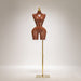 Mannequin torso on a stand with a gold base against a neutral background