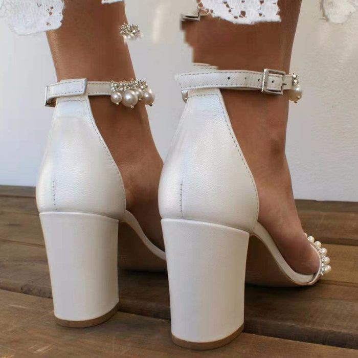 White high-heeled shoes with pearl embellishments on a wooden floor.
