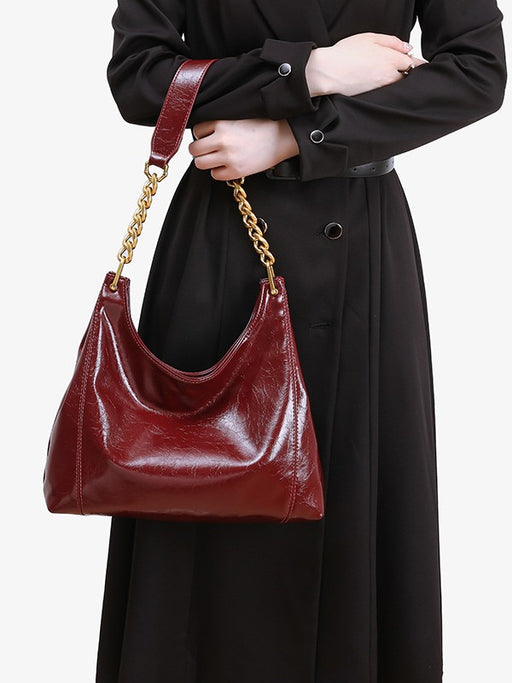 Person holding a red handbag with a gold chain strap against a plain background