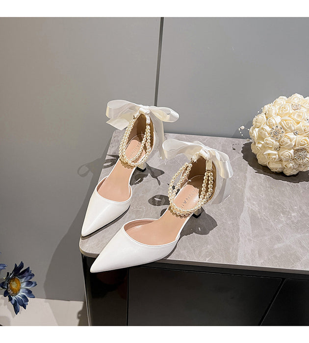 White high-heeled shoes with pearl details on a gray surface.