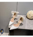 White high-heeled shoes with pearl details on a gray surface.