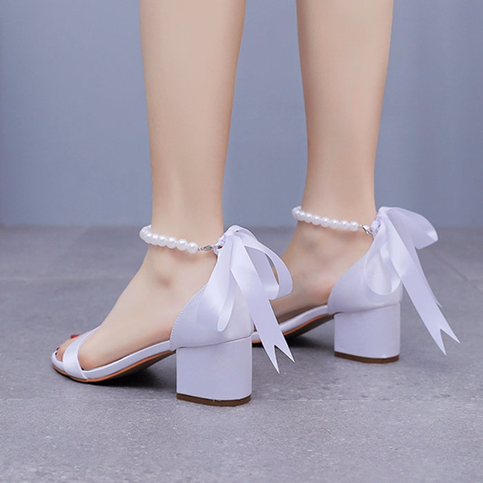 White sandals with ribbons and pearl anklets on a neutral background
