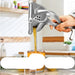 Handheld manual juicer squeezing orange juice into a glass with a blurred kitchen background.