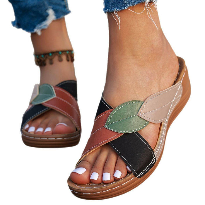 Colorful sandals with leaf patterns worn by a person on a white background