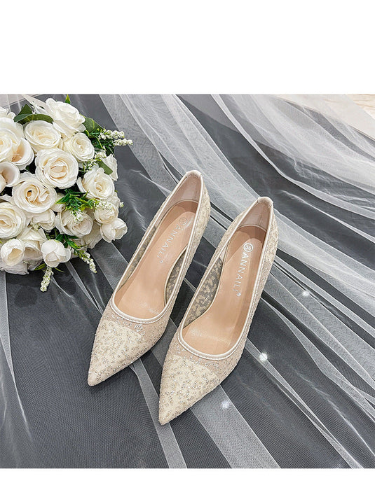 Pair of beige high-heeled shoes on a gray fabric background with white flowers.