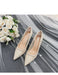 Pair of beige high-heeled shoes on a gray fabric background with white flowers.
