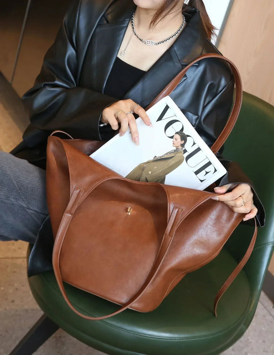 Person holding a brown leather bag with a 'Vogue' magazine inside, sitting on a green chair.