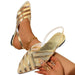 Gold strappy high-heeled shoes worn by a person on a white background