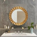 Gold circular mirror on a gray marble wall with bathroom decor.