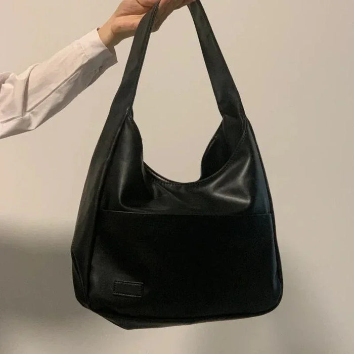 Black handbag held by a person against a plain background
