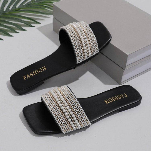 Black slides with pearl embellishments on a light surface with 'FASHION' branding.