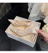 Beige high-heeled shoes in a box with a hand opening it, on a dark tiled floor.