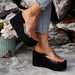Black wedge sandals with clear platforms worn by a person sitting against a stone wall.