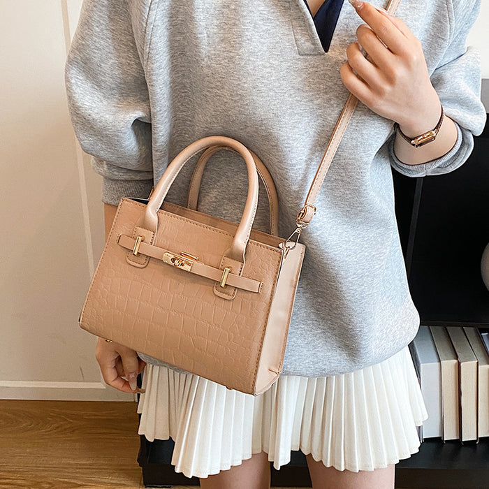 A woman wearing a gray sweatshirt and white pleated skirt carries a beige crocodile-embossed leather handbag with gold hardware.
