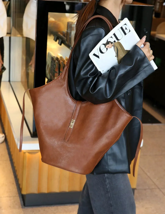 Person holding a brown leather tote bag and a magazine with a visible brand logo.