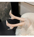 High-heeled shoes worn with a light-colored dress on a dark marble floor.
