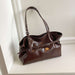 A dark brown glossy leather handbag with double shoulder straps and a front buckle strap, resting on a white shelf against a white wall.