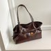 A dark brown glossy leather handbag with double shoulder straps and a front buckle strap, resting on a white shelf against a white wall.