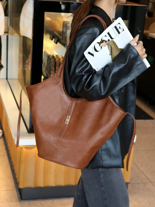 Person holding a brown leather tote bag and a magazine with a visible brand logo.