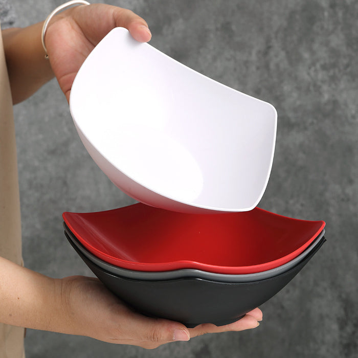 Person holding a stack of white, red, and black ceramic bowls against a gray background