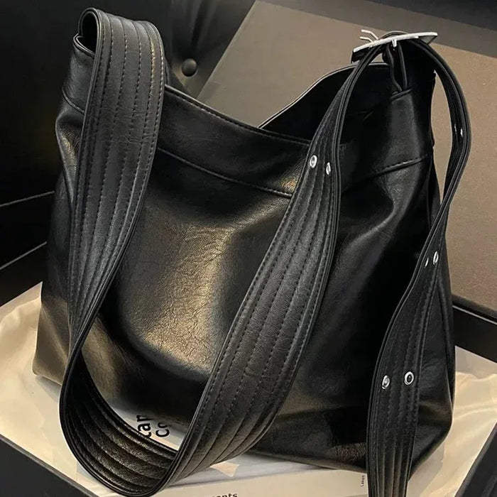 Black leather handbag with a long strap on a neutral background