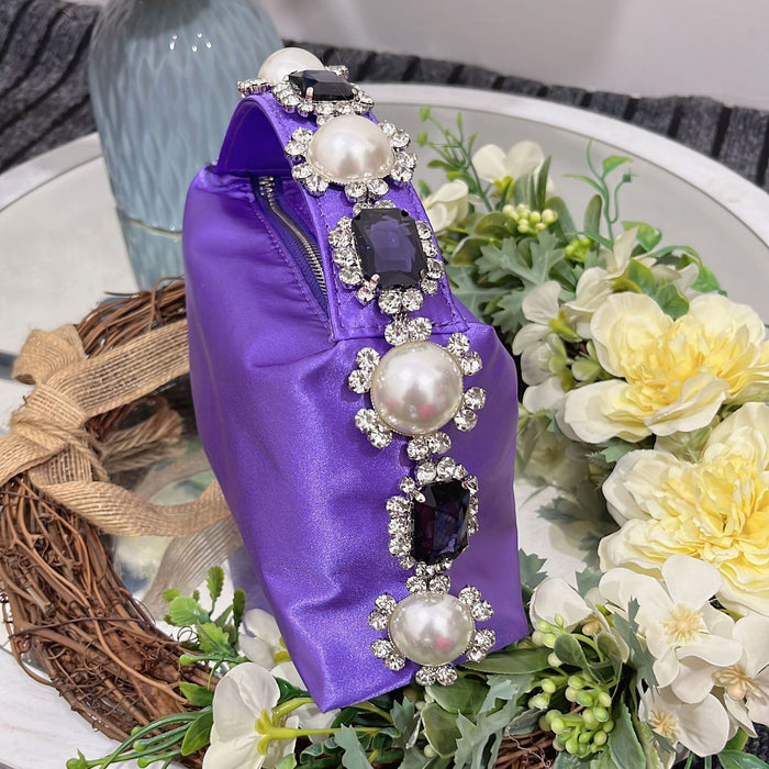 Purple handbag with decorative pearls and gemstones on a floral and woven mat background