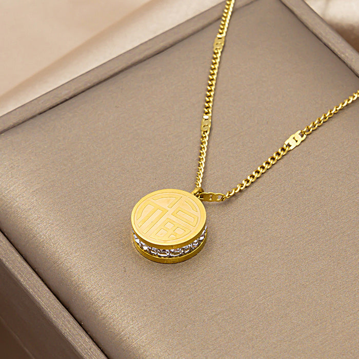 A gold pendant necklace with a circular emblem and a small row of clear stones, displayed on a beige jewelry box.