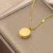 A gold pendant necklace with a circular emblem and a small row of clear stones, displayed on a beige jewelry box.