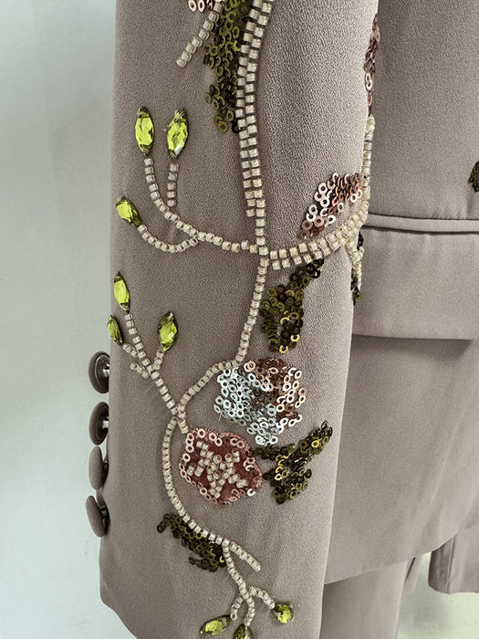 Close-up of a beige garment with intricate bead and sequin embroidery on a plain background