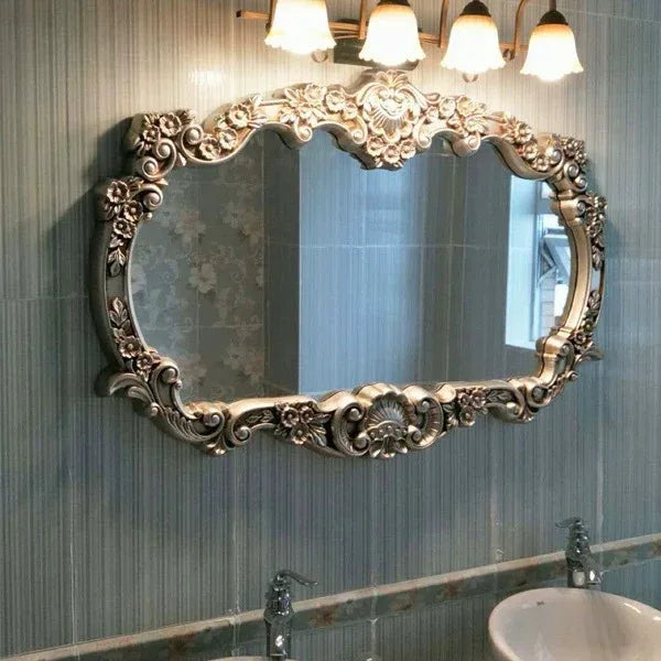 Decorative oval mirror with intricate gold frame above a sink in a bathroom.