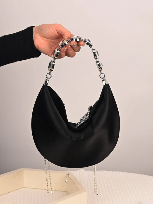 Black handbag with chain handle held by a hand against a neutral background