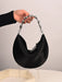 Black handbag with chain handle held by a hand against a neutral background