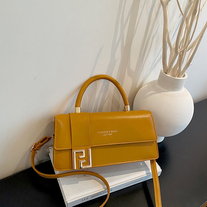 A mustard yellow faux leather handbag with a top handle, a long shoulder strap, and a prominent gold-toned double-F logo clasp, resting on a white book next to a white textured vase.