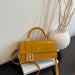 A mustard yellow faux leather handbag with a top handle, a long shoulder strap, and a prominent gold-toned double-F logo clasp, resting on a white book next to a white textured vase.