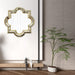 Decorative mirror with geometric frame on a wall next to a potted plant.