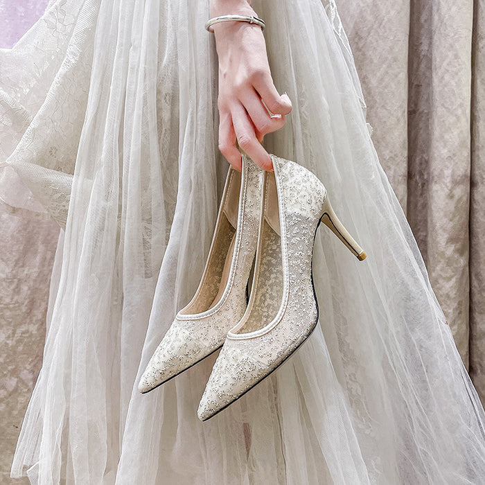 Pair of sparkly high-heeled shoes held by a hand against a light background